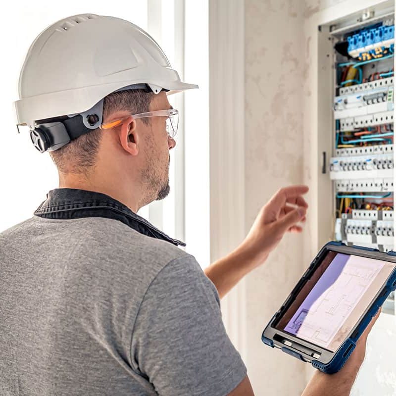 man-electrical-technician-working-switchboard-with-fuses-uses-tablet