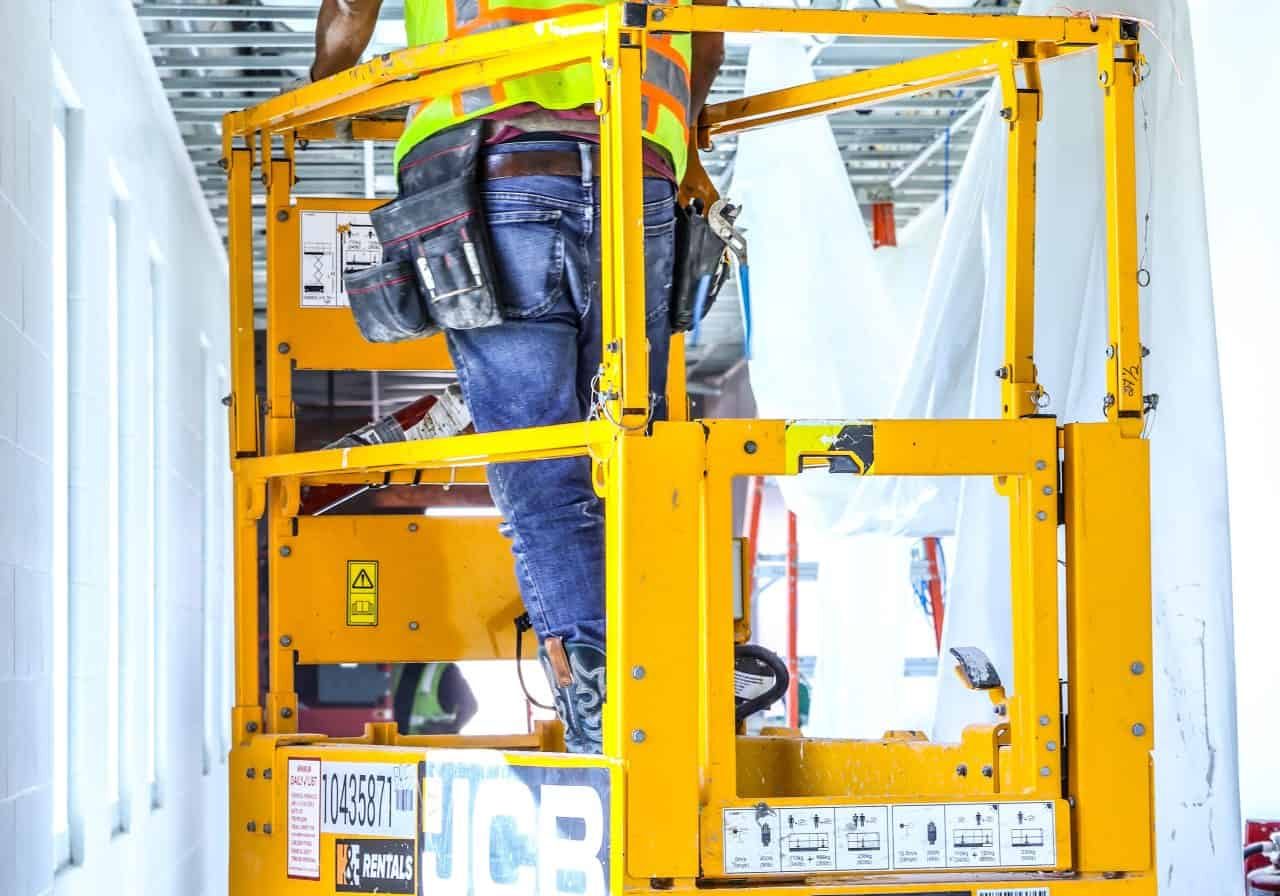 High-visibility safety gear, working on ceiling wiring installation, electrical work, construction site.